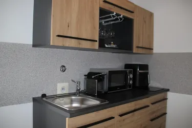 Eine moderne Kücheneinheit mit Holzfronten und Edelstahlgeräten. Die Küche verfügt über ein Waschbecken, eine Mikrowelle und eine Kaffeemaschine.