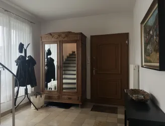 Ein einladender Flur mit einem Holzschrank, einer Garderobe und einer Treppe. Helle Vorhänge lassen Licht herein und schaffen eine freundliche Atmosphäre.