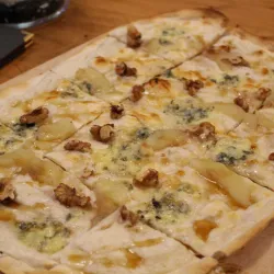 Ein leckerer Flammkuchen mit Walnüssen, Birnen und Käse. Die rustikale Holzplatte unterstreicht die appetitliche Präsentation.