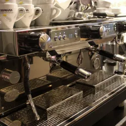 Eine moderne Kaffeemaschine mit glänzendem Edelstahl und mehreren Tassen. Im Hintergrund sind weitere Kaffeetassen und Zubehör sichtbar.