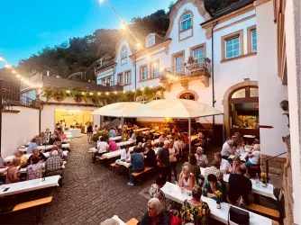 Eine belebte Innenhofgaststätte mit vielen Tischen und Gästen. Lichterketten sorgen für eine gemütliche Atmosphäre am Abend.