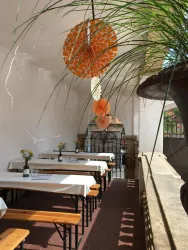Ein helle, gemütliche Terrasse mit langen Holztischen und Bänken. Bunte Dekorationen hängen von der Decke und es sind Blumen auf den Tischen.