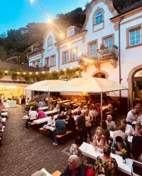 Ein belebter Außenbereich eines Restaurants mit vielen Gästen. Die Atmosphäre ist festlich und es gibt Tische unter Markisen.