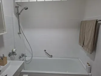 Ein modernes Badezimmer mit einer Badewanne und einer Duschvorrichtung. Handtücher hängen an der Wand und das Licht ist hell.