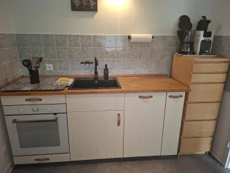 Eine moderne Küche mit einem Holzarbeitsplatten und grauen Fliesen. Die Ausstattung umfasst einen Herd, eine Spüle und einen Kaffeebereiter.