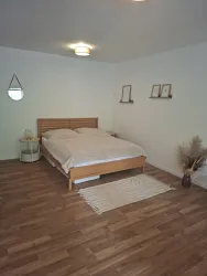 Ein helles Schlafzimmer mit einem Doppelbett und Holzfußboden. An den Wänden hängen einige Bilder und eine kleine Spiegel.