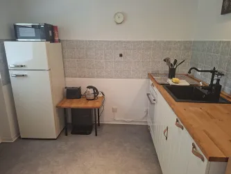 Eine moderne Küche mit einem Kühlschrank, einem Holzarbeitsplatz und einem Waschbecken. Die Wände sind hell gefliest und es gibt eine Wanduhr.