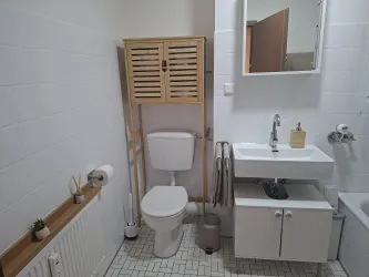 Ein modernes Badezimmer mit hellem Fliesenboden und funktionalen Möbeln. Die sanitären Einrichtungen sind ordentlich angeordnet, und es gibt dekorative Pflanzen.