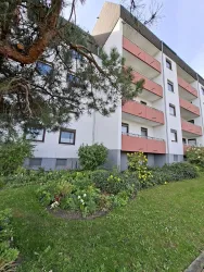 Ein modernes Wohngebäude mit mehreren Balkonen und umgebenden Pflanzen. Der Garten wirkt gepflegt und einladend.