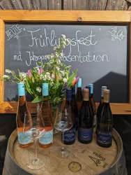 Ein Frühlingsfest mit einer Präsentation von Jahrgängen. Im Vordergrund stehen Weinflaschen und Gläser, umgeben von frischen Blumen.