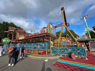 Ein buntes Freizeitpark-Attraktion mit Karussells und Achterbahn. Menschen gehen entlang der Wege und genießen die Atmosphäre.