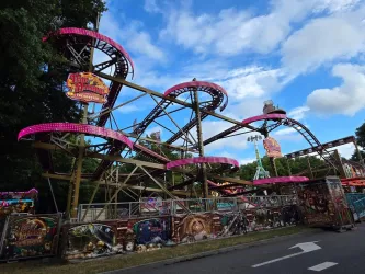 Eine große Achterbahn mit bunten Lichtern und einer spannenden Struktur. Der Himmel ist blau mit einigen Wolken.