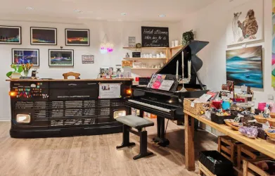 Ein gemütlicher Raum mit einem Klavier und einem Empfangstresen. Wanddekorationen und Geschenktische schaffen eine einladende Atmosphäre.