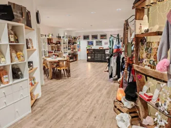 Ein einladendes Geschäft mit Regalen voller Lebensmittel und Waren. An der Seite hängen Schmuck und Bekleidung, während Tische zum Sitzen einladen.