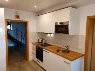 Eine moderne Küche mit weißen Schränken und Holztischplatte. Im Hintergrund ist eine Treppe zu sehen.