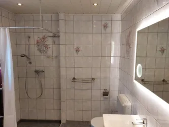 Ein modernes Badezimmer mit einem Duschbereich und einem weißen Waschbecken. Die Wände sind mit weißen Fliesen und floralem Muster dekoriert.