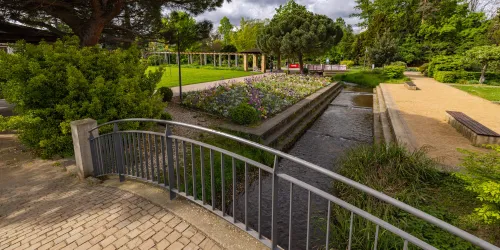 Ein schöner Park mit einem kleinen Fluss und bunten Blumenbeeten. Es gibt Wege und Bänke zum Entspannen.