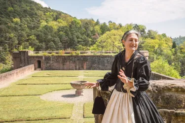 Eine Frau in historischer Kleidung steht in der Hardenburg bei Bad Dürkheim. Im Hintergrund sind grüne Wiesen und Bäume zu sehen.