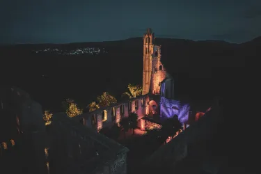 Eine alte Ruine mit beleuchteten Mauern in der Nacht. Die Umgebung ist dunkel, und das Licht erzeugt eine geheimnisvolle Atmosphäre.