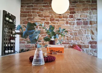 Ein stilvoller Raum mit einer Steinwand und einem großen runden Licht. Auf dem Holztisch stehen Pflanzen und eine dekorative Box.