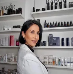 Eine Frau in einem weißen Blazer steht vor Regalen mit verschiedenen Hautpflegeprodukten. Im Hintergrund sind zahlreiche Produkte der Marke Babor zu sehen.