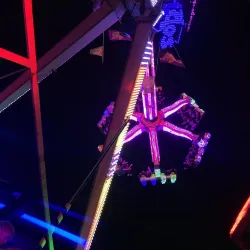 Ein bunte Lichtinstallation von einem Fahrgeschäft auf einem Jahrmarkt. Menschen genießen die Fahrt unter dem Nachthimmel.