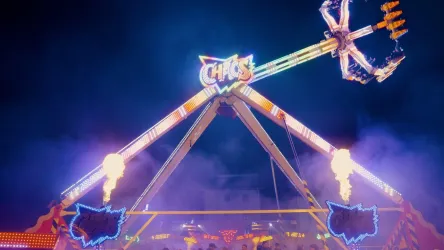 Ein aufregendes Fahrgeschäft auf einem Jahrmarkt, beleuchtet mit bunten Lichtern. Es gibt Flammen und eine festliche Stimmung in der Nacht.