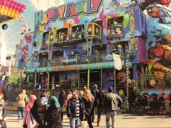 Ein bunter Freizeitpark mit einem Gebäude namens „Happy Family“. Viele Menschen besuchen die Attraktion und genießen die fröhliche Atmosphäre.