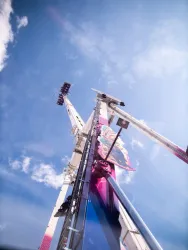 Ein großes Fahrgeschäft ragt in den Himmel. Der klare blaue Himmel und die wenigen weißen Wolken machen die Szene lebhaft.