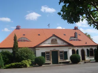 Ein Weingut mit einem schönen, roten Ziegeldach und einer einladenden Fassade. Umgeben von grünen Büschen und unter blauem Himmel.