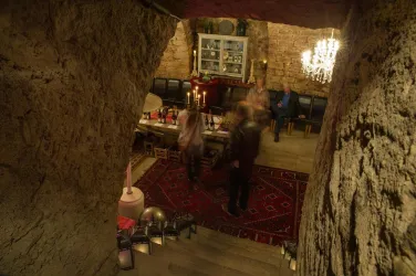 Ein stilvoller Kellerraum mit einer festlichen Tafel und einer prachtvollen Deckenleuchte. Gäste sind sichtbar und schaffen eine lebendige Atmosphäre.