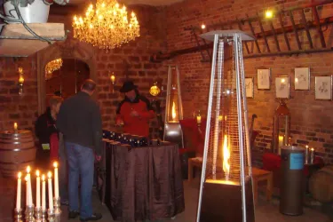 Ein gemütlicher Raum mit warmem Licht und einem Kronleuchter. Menschen stehen um einen Tisch mit Getränken und Heizstrahlern.