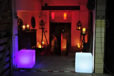 Ein stimmungsvolles Ambiente mit bunten Leuchten und Kerzen. Im Hintergrund führt eine Treppe in einen dunkleren Raum.