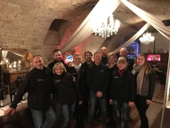 Eine Gruppe von Menschen steht in einem stilvollen Raum mit einem gemütlichen Ambiente. Die Einrichtung umfasst Kristallleuchter und dekorative Elemente.