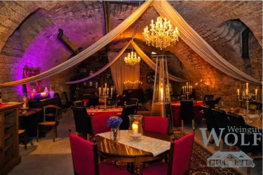 Ein stilvolles Restaurant in einem historischen Weinkeller mit eleganten Tischen und roten Stühlen. Die Atmosphäre wird durch Kronleuchter und sanfte Beleuchtung verstärkt.