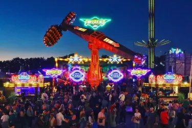 Ein aufregender Jahrmarkt mit bunten Fahrgeschäften und heller Beleuchtung. Menschen genießen die Attraktionen unter dem nächtlichen Himmel.