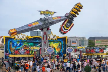 Eine lebhafte Jahrmarktattraktion mit einer großen, schwingenden Fahrgeschäfte. Viele Menschen versammeln sich vor dem bunten Stand.