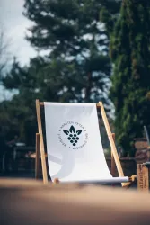 Ein bequemer Liegestuhl mit einem weißen Stoff und einem Logo. Im Hintergrund sind Bäume und eine natürliche Umgebung sichtbar.