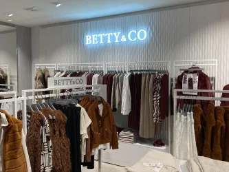 Ein moderner Bekleidungsladen mit einer Auswahl an Herbstmode. An der Wand leuchtet ein Schild mit dem Namen "BETTY & CO".