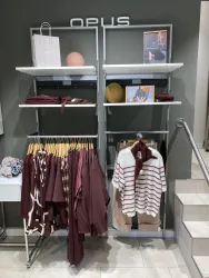 Ein modernes Verkaufsregal mit Kleidung in verschiedenen Rot- und Beigetönen. Auf den Regalen sind auch Accessoires und Dekorationsartikel zu sehen.