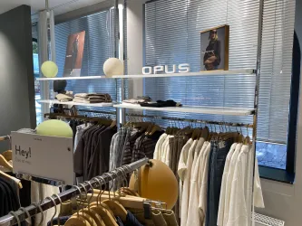Ein eleganter Bekleidungsraum mit Regalen voller Kleidung. Das Logo "OPUS" ist prominent sichtbar, und einige dekorative Elemente sind im Raum platziert.