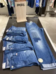 Eine Auswahl an Jeans in verschiedenen Größen und Stilen liegt auf einem Tisch. Im Hintergrund steht ein Holzschild mit der Aufschrift "ANGELS".