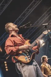 Ein Musiker spielt Gitarre und singt auf einer Bühne. Die Stimmung ist lebhaft und energisch.