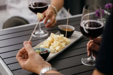 Eine elegante Tafel mit Gläsern Rotwein und einem Teller mit Käsewürfeln. Dazu gibt es kleine Schälchen mit Dips und frischen Blumen.