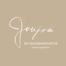 Das Bild zeigt das Logo der Marke "Joujou", die sich auf biologische, vegane und glutenfreie Backwaren spezialisiert hat. Der Hintergrund ist beige und das Schriftbild ist in eleganten Weißtönen gehalten.