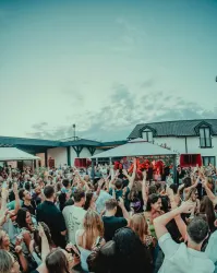 Eine große Menschenmenge feiert bei einem Open-Air-Konzert. Viele Leute tanzen und haben Spaß unter einem klaren Himmel.
