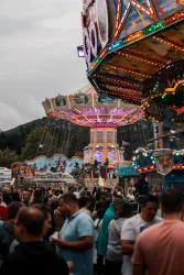 Ein belebter Jahrmarkt mit bunten Fahrgeschäften und vielen Menschen. Lichter funkeln und schaffen eine festliche Atmosphäre.