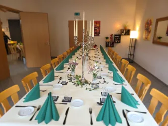 Ein festlich gedeckter Tisch mit grünen Servietten und Kerzenhaltern. Der Raum ist hell und einladend.