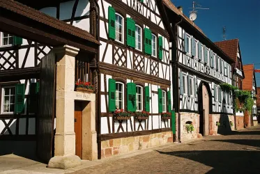 Eine malerische Straße mit Fachwerkhäusern und grünen Fensterläden. Die Gebäude strahlen einen charmanten, historischen Charakter aus.