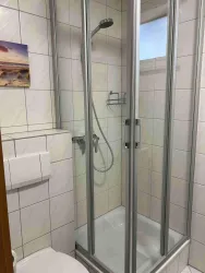 Eine moderne Dusche mit Glastür und einer Regenschauerdusche. Die Wände sind mit hellen Fliesen gefliest.